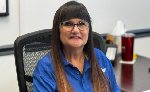 Smiling woman with glasses in a blue shirt seated at an office desk