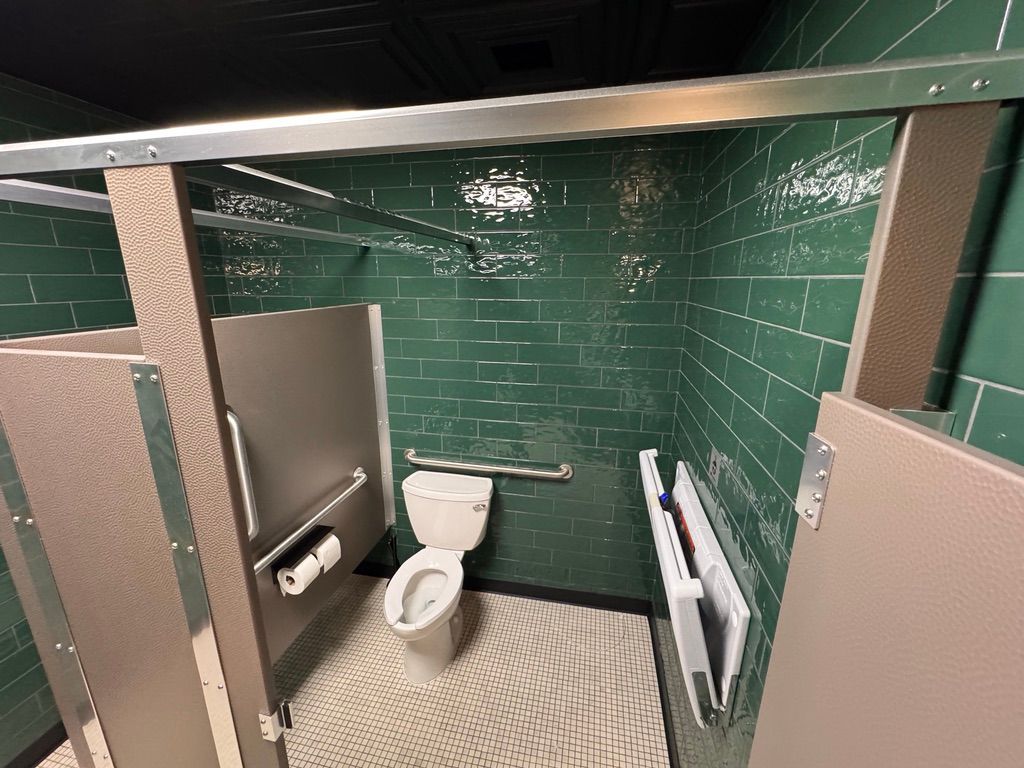 Accessible restroom stall with toilet, grab bars, teal tiled walls, and privacy partitions