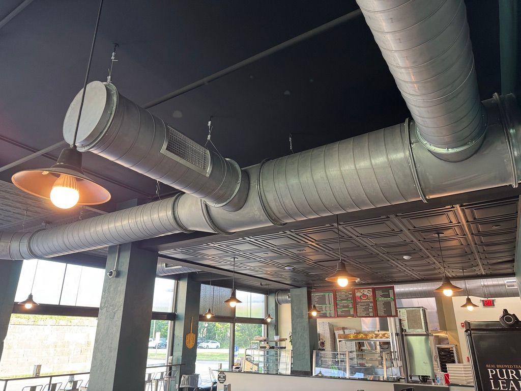 Industrial café interior with exposed ductwork, hanging lights, and large windows
