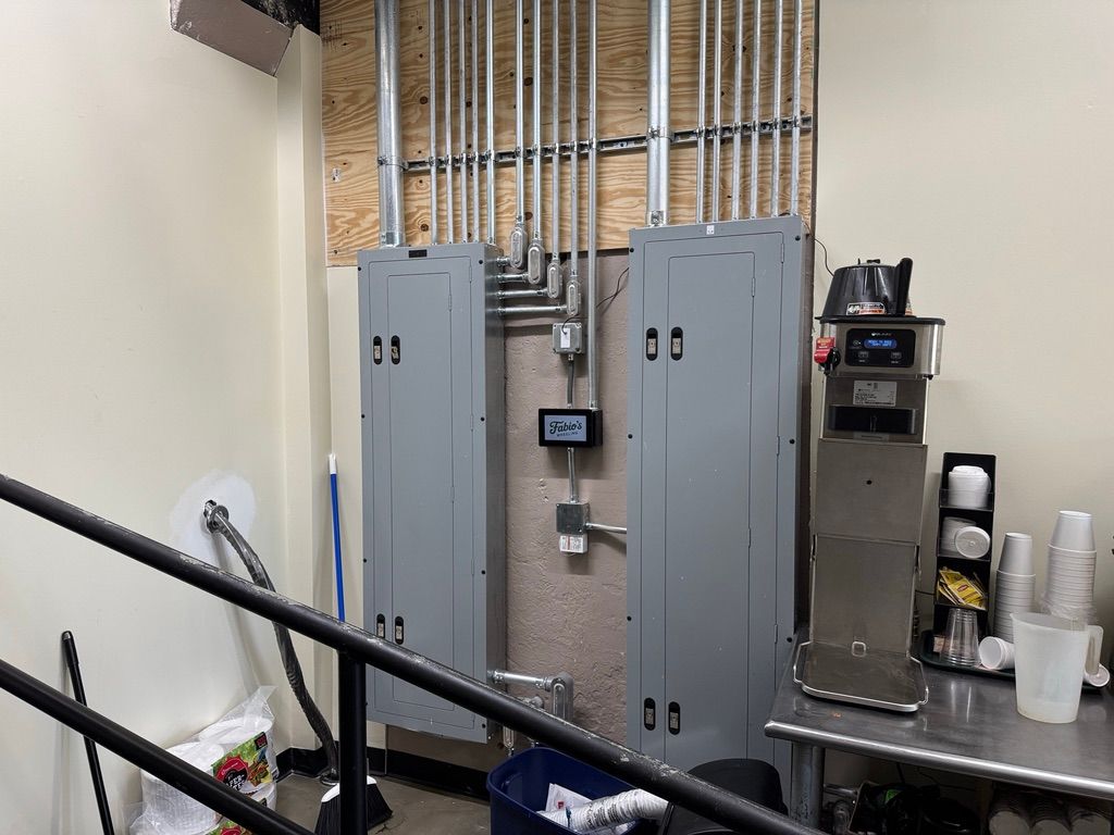 Utility room with gray electrical panels, exposed conduit, and stainless steel equipment on the right.
