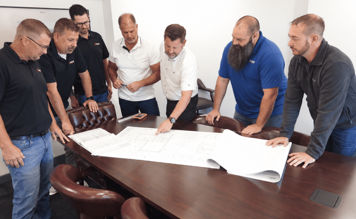 Group of people gathered around a conference table, reviewing large architectural plans together