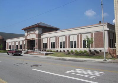 Low brick civic building with arched windows and a parked car along a street under a blue sky
