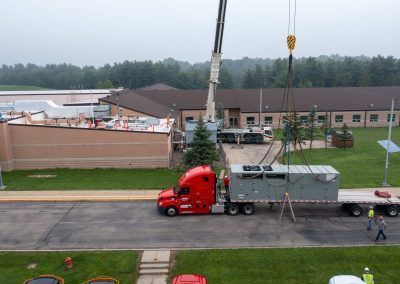 Red semi-truck parked by a crane at a building site beside a large brick building
