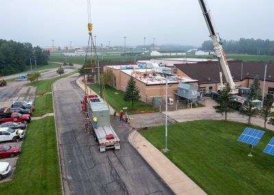 Aerial view of a construction site with cranes, workers, and trucks beside a road and parking lot