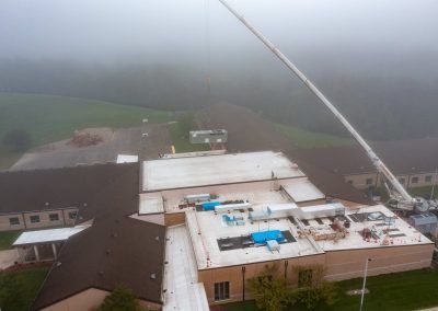 Aerial view of a large white-roofed building in fog, with a crane and fields in the background.
