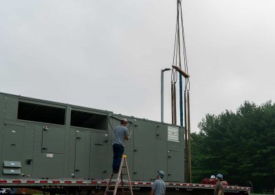 Workers rigging a large green generator unit onto a truck at an outdoor site