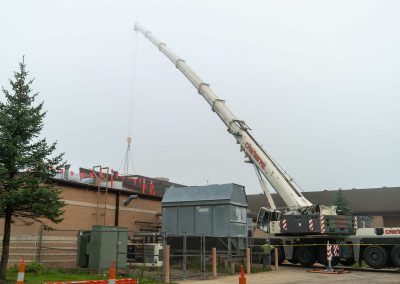 Crane lifting a modular structure beside a brick building on an overcast construction site