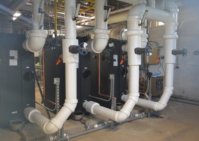 Industrial mechanical room with large white pipes, valves, and equipment along a concrete floor
