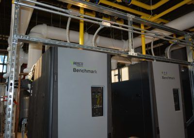 Industrial equipment room with two gray Benchmark units and overhead yellow piping