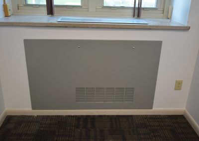 Gray wall-mounted radiator cover beneath a window in a carpeted room