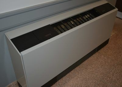 White wall-mounted heater beneath a window in a carpeted room