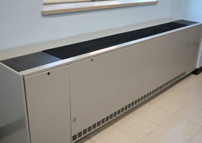 Long white radiator cover along a wall, with a black top and vented base in a hallway.
