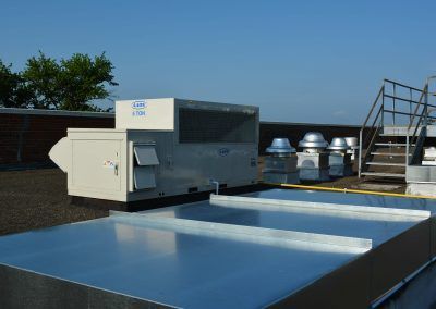 Rooftop HVAC equipment and vents beside a reflective blue surface under a clear sky
