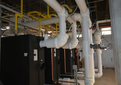 Industrial room with black equipment and white pipes overhead, with yellow pipes in the background