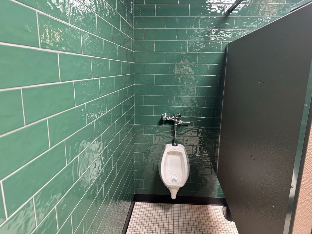 Green tiled restroom with a urinal between a wall and privacy partition
