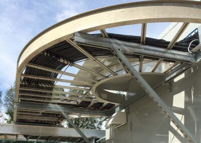 Curved steel roof frame under construction, with exposed beams against a blue sky.