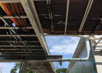 Underside of a modern pedestrian bridge with metal beams and a blue sky above