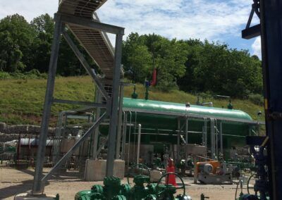 Industrial site with green tanks, metal stairs, and equipment under a cloudy sky