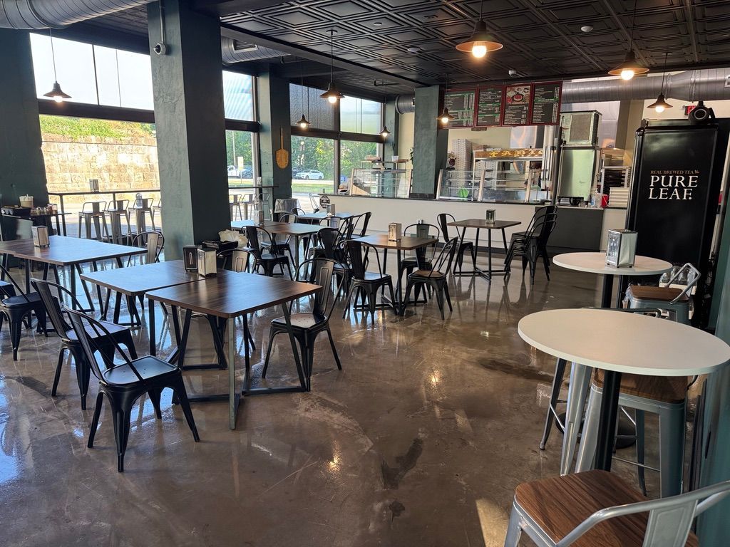 Empty modern café with scattered black tables and chairs, polished concrete floor, and large windows.