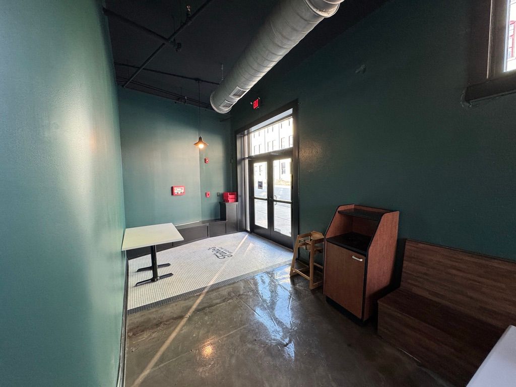 Empty teal hallway with glass doors, bench seating, and industrial ceiling ductwork