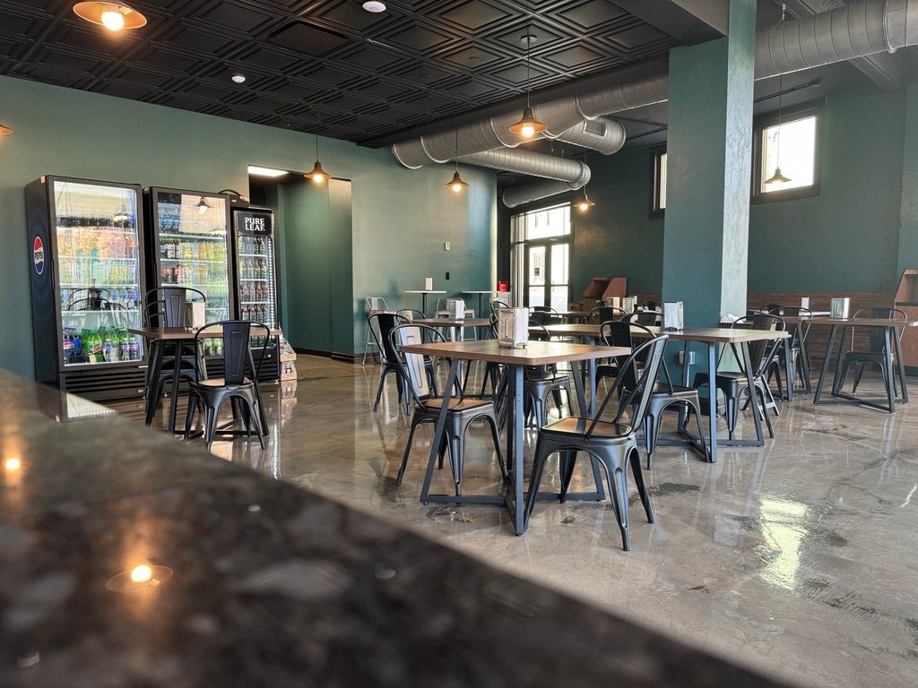 Modern cafe interior with empty tables, black chairs, teal walls, and glass-front drink coolers