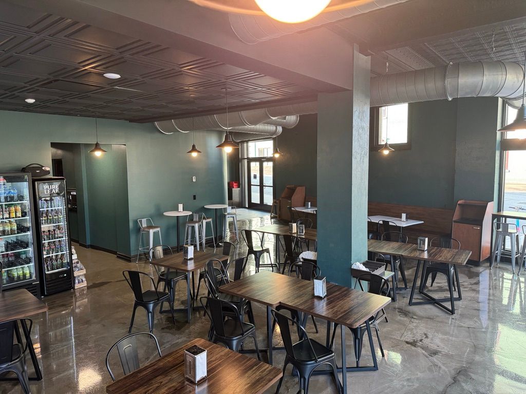 Empty modern café with tables, chairs, and a beverage cooler under warm ceiling lights.