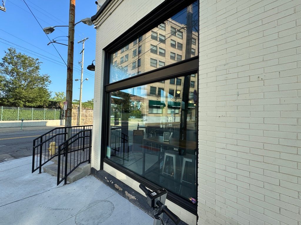 Storefront with large windows and a black metal ramp beside a sidewalk on a sunny street