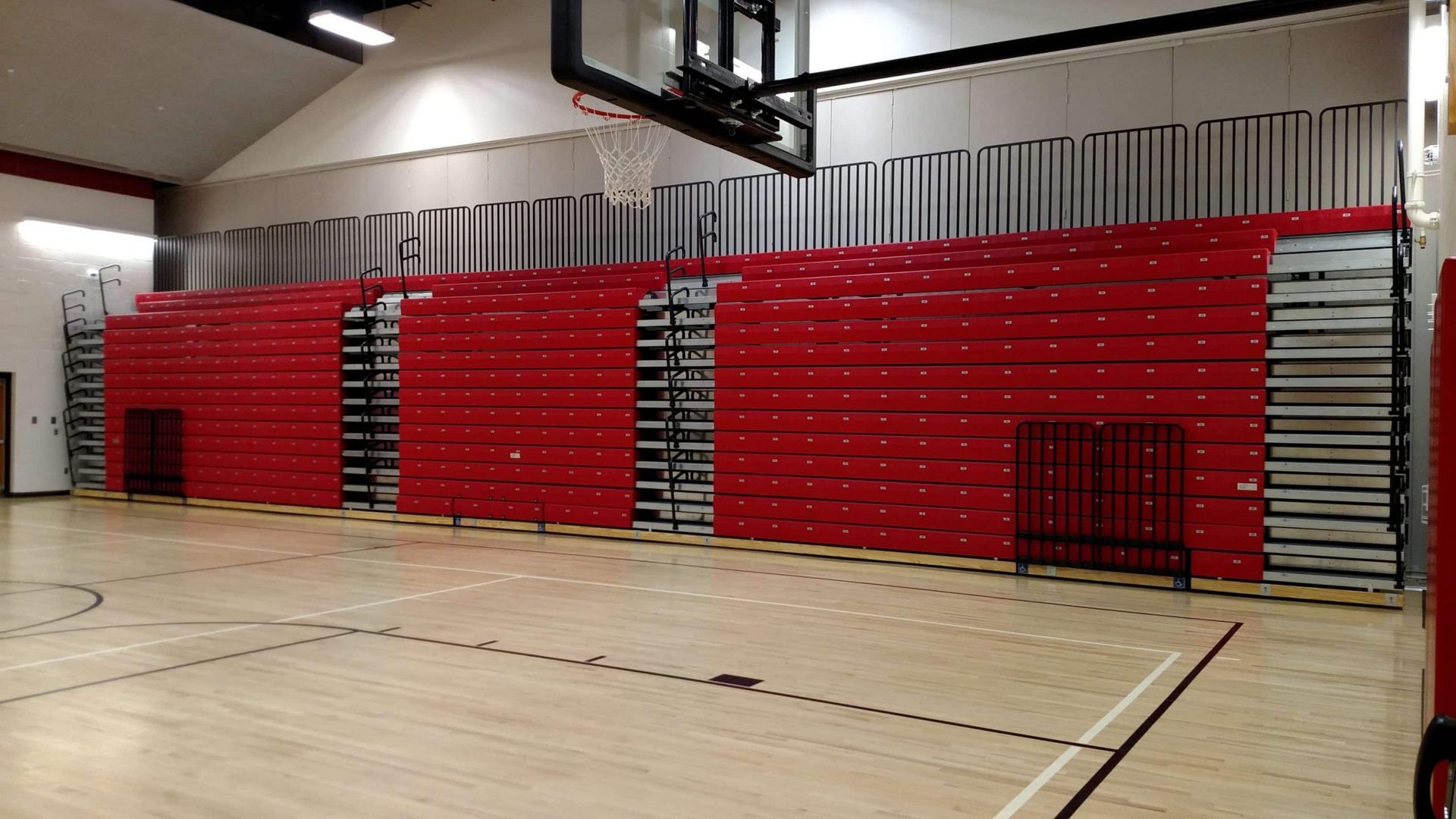 Indoor gym with red retractable bleachers against a wall on a basketball court
