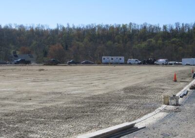 Gravel parking lot beside a wooded area, with parked vehicles and traffic cones under a clear sky