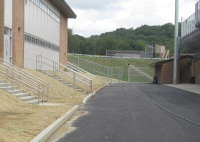 Empty paved path beside a building with metal stairs and railings, leading toward a grassy hillside