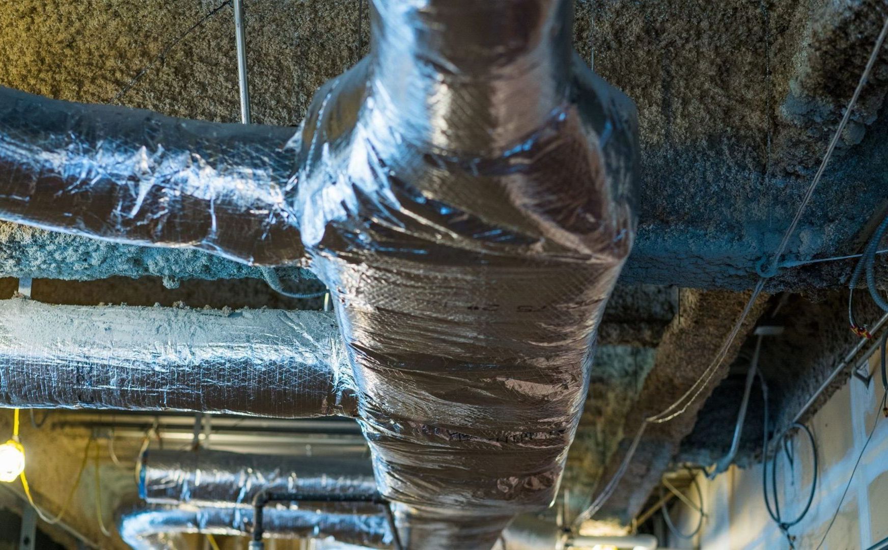 Insulated HVAC ducts and pipes running across a ceiling in a building interior