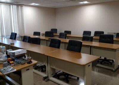 Empty conference room with long tables, black chairs, and projector equipment near the front.