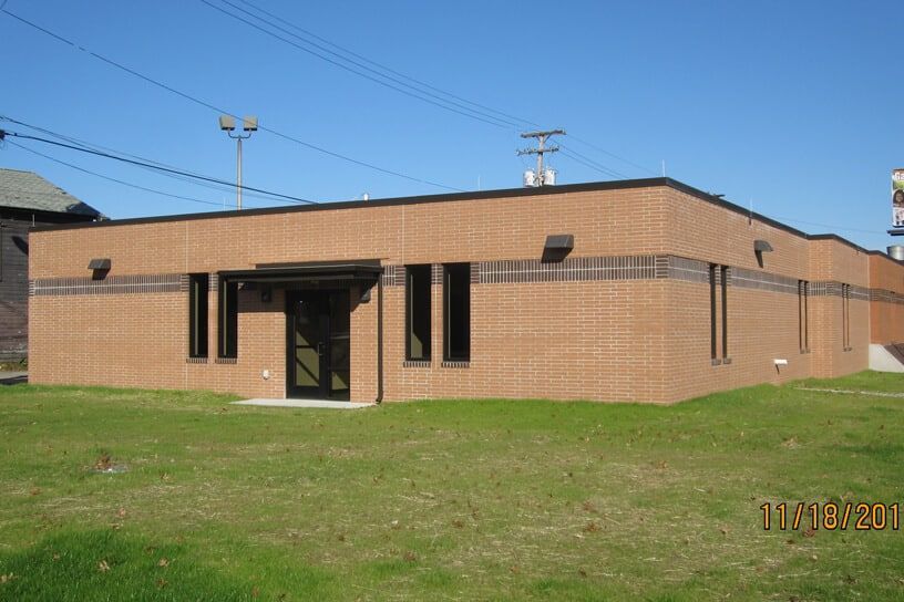 Single-story brick building with a black entrance door and grassy lawn under a clear sky