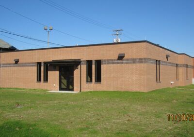 Single-story brick building with a dark entrance, set on a grassy lawn under a blue sky.