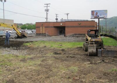 Construction site with excavator and bulldozer beside a brown building under overcast skies