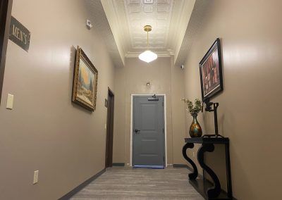 Narrow hallway with beige walls, framed art, a blue door, and a black console table with flowers.