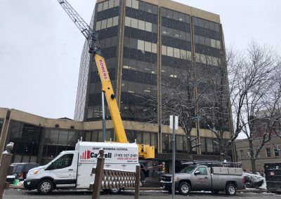 Yellow crane truck lifting near a dark office building on a snowy street