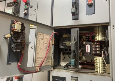 Open electrical control panel with wiring, switches, and relays inside a metal cabinet.