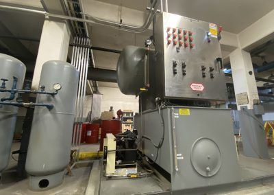 Industrial boiler room with large gray tanks, pipes, and control panels inside a mechanical basement.