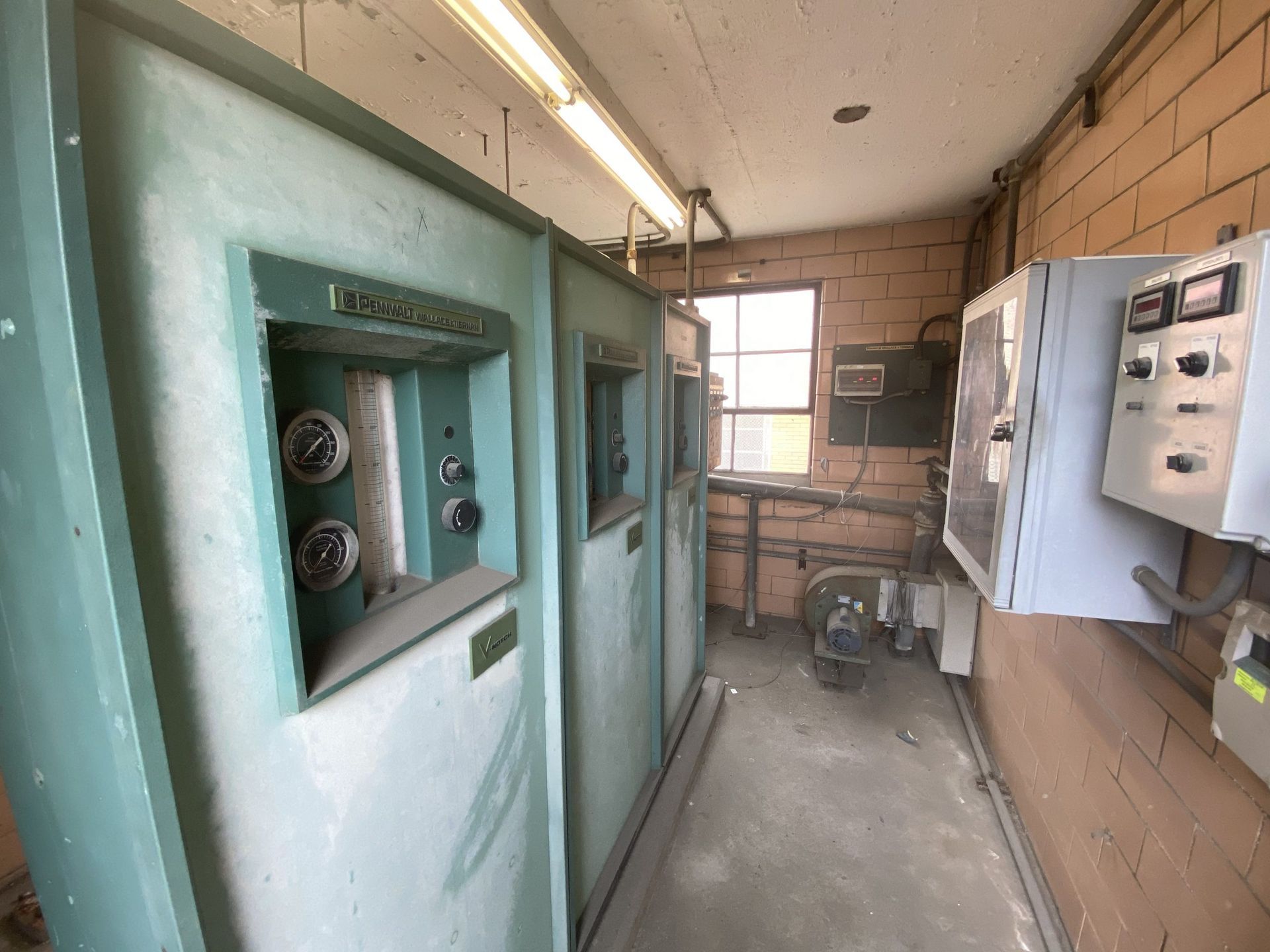 Industrial electrical room with turquoise cabinets, wall-mounted control panels, and exposed brick walls