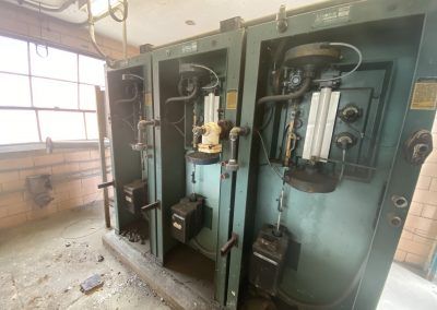 Old industrial control panels and machinery in a dusty utility room with large windows