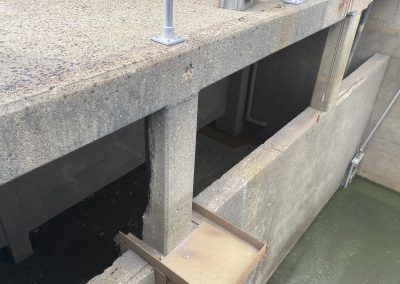 Concrete waterfront structure with open sluice gates above green water.