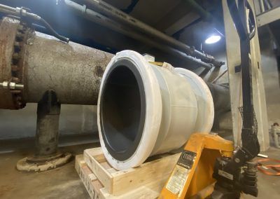Large white industrial pipe fitting on a pallet in a factory workshop, with machinery in the background