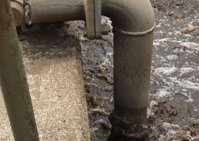 Rusty metal pipes over rough concrete beside muddy water.