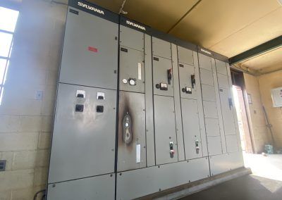 Industrial electrical control panel cabinets in a utility room with gray metal doors and gauges.