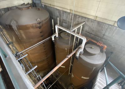 Two large brown industrial tanks with white piping in a concrete utility room.