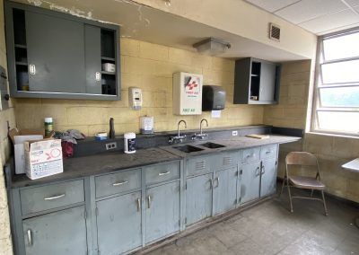 Kitchen with long gray counters, cabinets, sink, and a chair by a bright window.