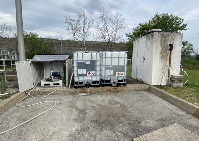Outdoor utility area with two storage tanks, a small shed, and coiled hoses on pavement.