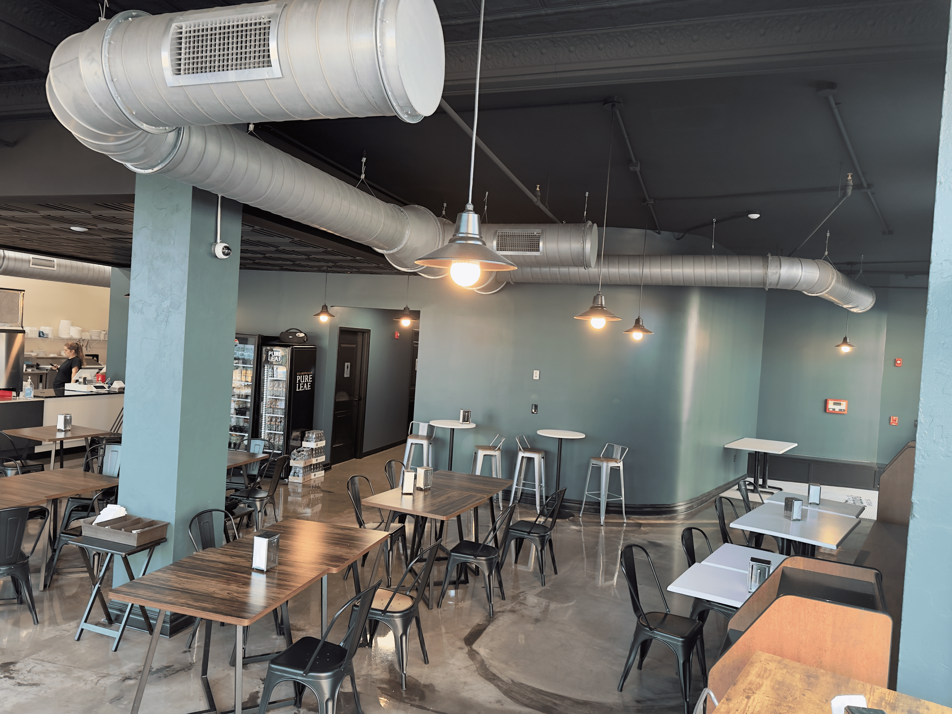 Industrial-style café interior with exposed ducts, hanging lights, and empty tables and chairs