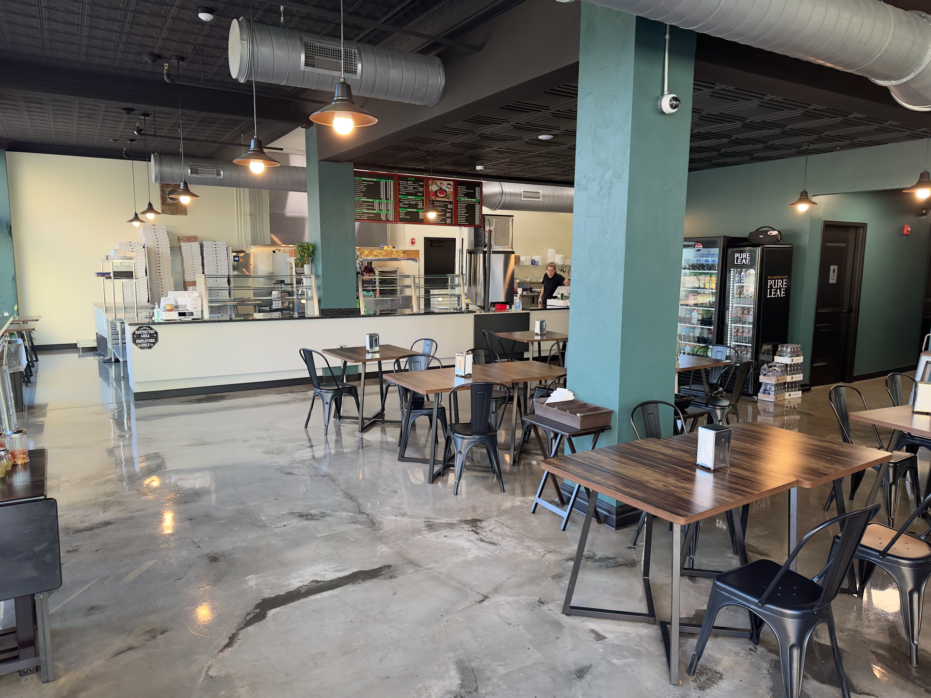 Empty modern café interior with tables, chairs, and a long white counter under exposed ducts.